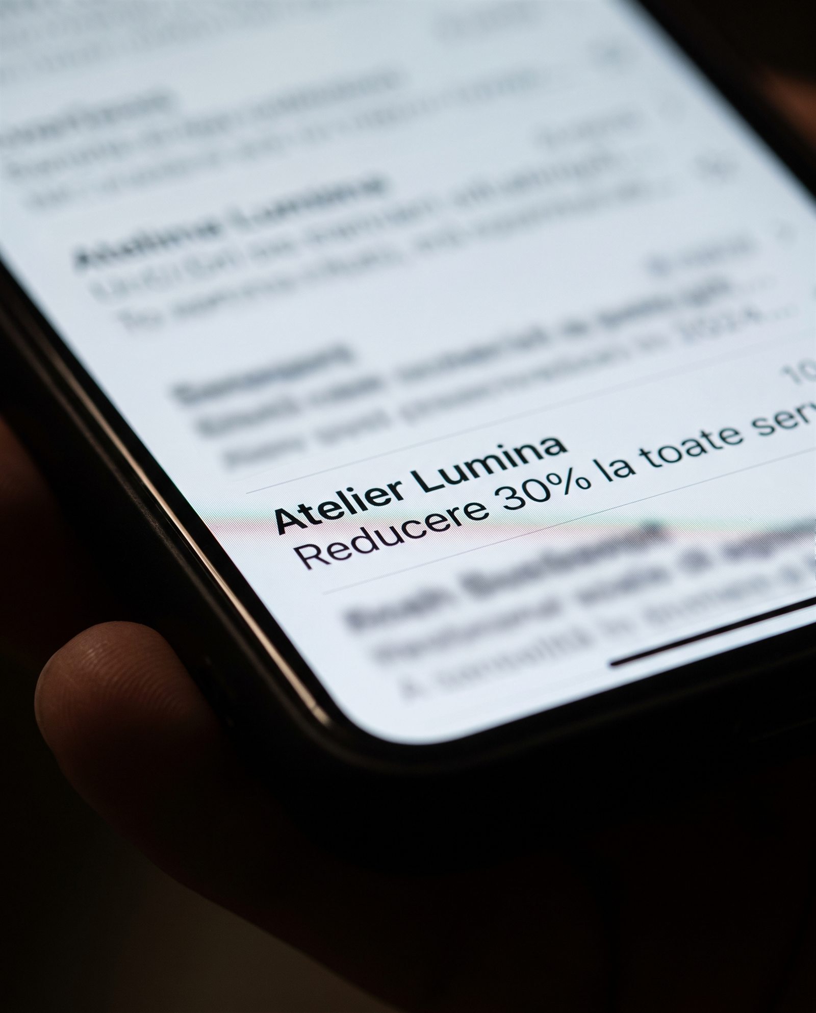 Pe ecranul unui smartphone apare un e-mail de la Atelier Lumina cu subiectul „Reducere de 30% la toate”, care sugerează o reducere de 30% la toate articolele. Mesajul este în limba română, iar fundalul este estompat.